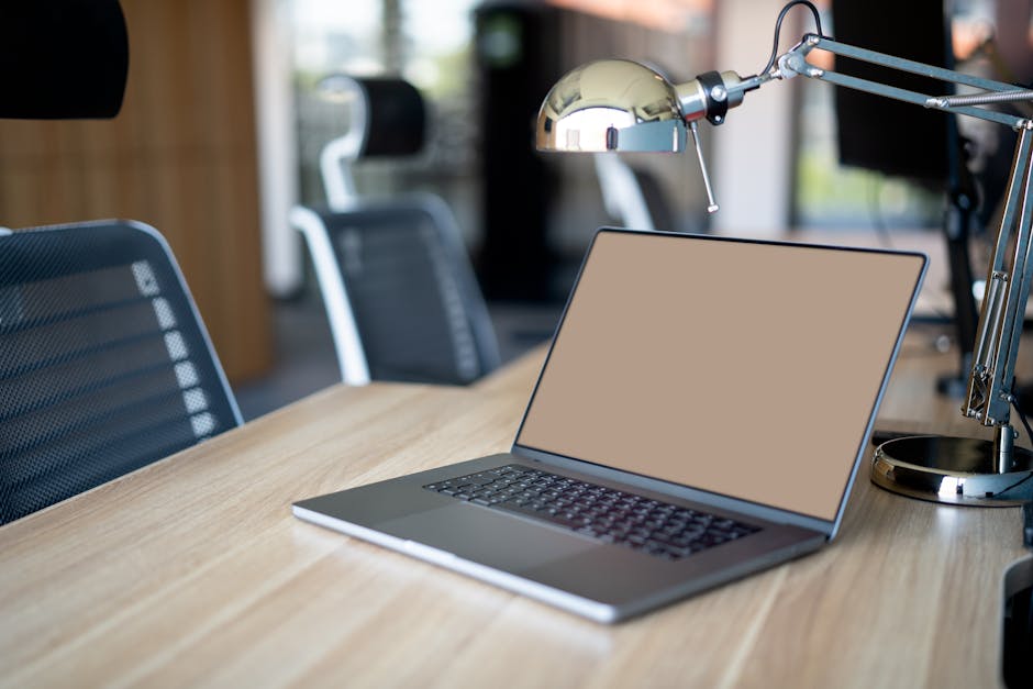 A sleek office setup featuring a laptop on a wooden desk with chairs and a metallic lamp.