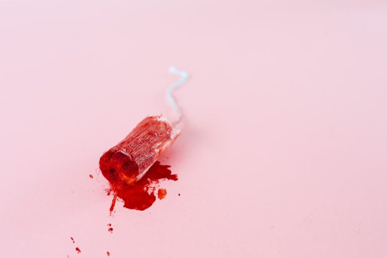Close-up image of a blood-stained tampon on a pink background symbolizing menstruation.