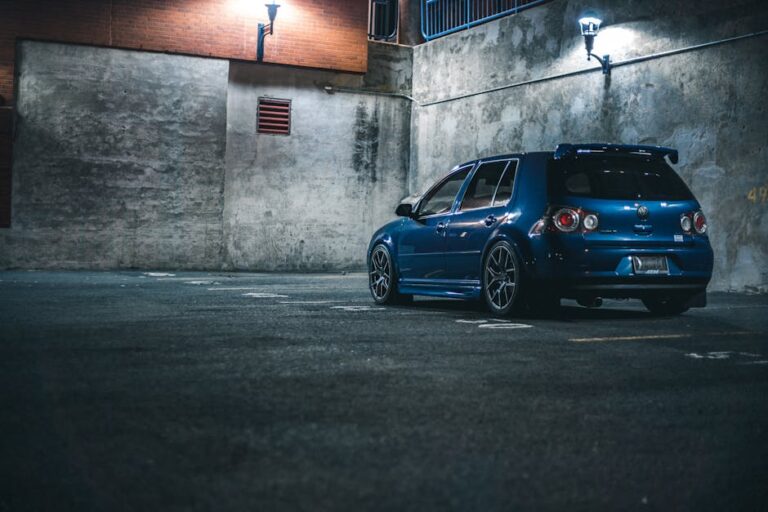 Blue hatchback automobile with spoiler parked on asphalt with marking lines near stone barrier in city street in evening time
