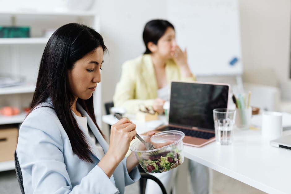 Asian woman enjoying a salad during a lunch break in a modern office workspace.
