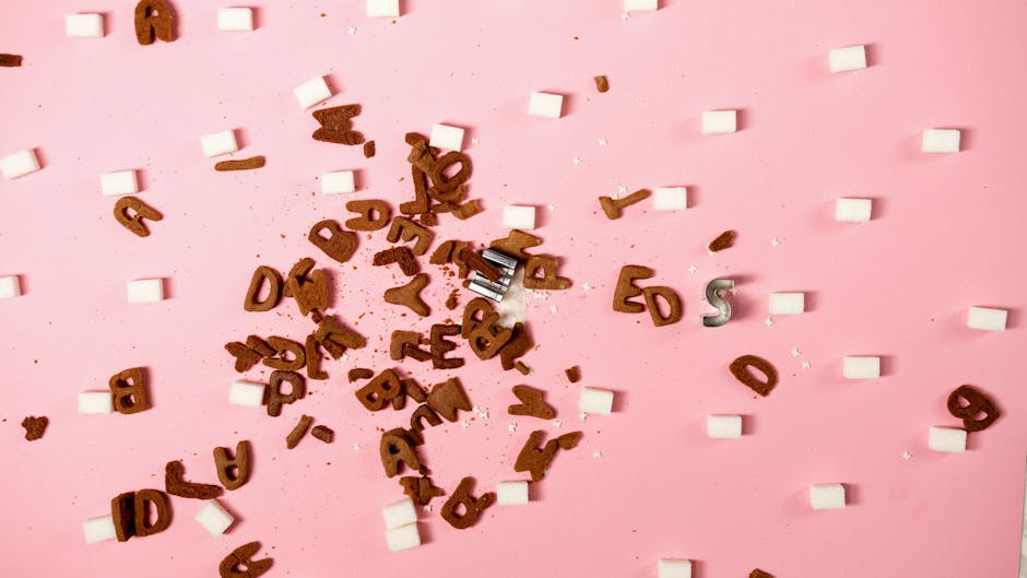 Scattered letters and sugar cubes on a pink background creating an artistic concept.