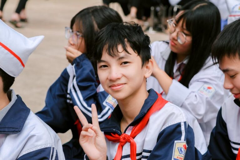 Smiling Asian students in uniforms, outdoor school event, peace sign.