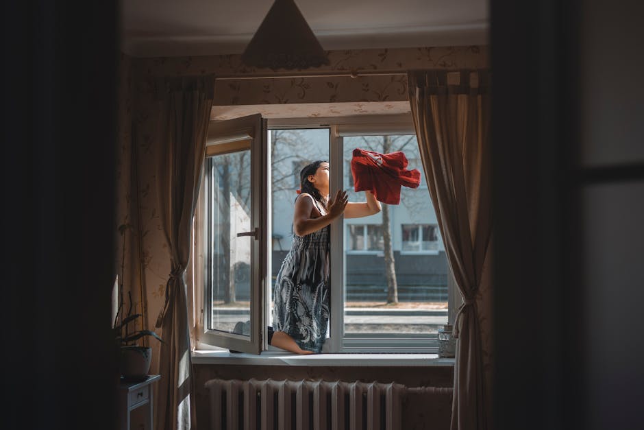 A woman cleaning a window in a well-designed cozy apartment with curtains and natural light.
