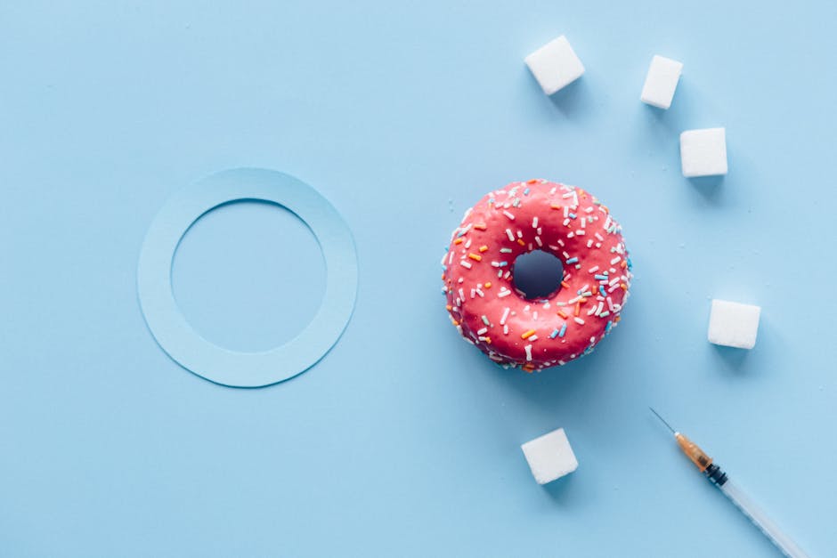 Flat lay of a pink donut, sugar cubes, and syringe on a blue background symbolizing diabetes awareness.