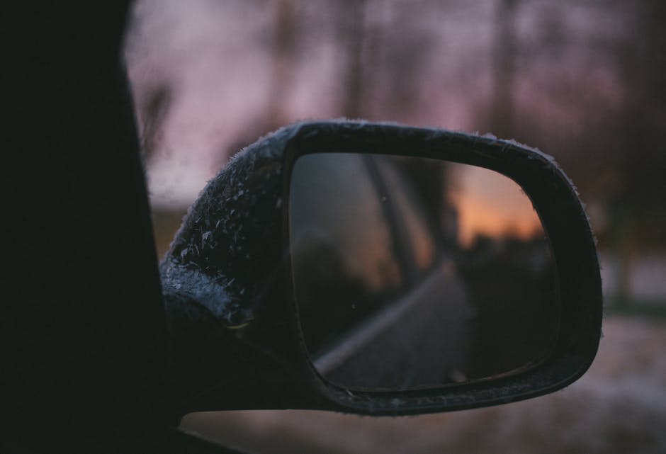 Close-up of a frosty car mirror reflecting a serene winter sunset.