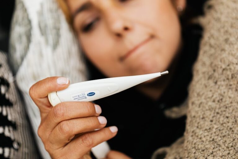 Close-up of a woman holding a digital thermometer, feeling unwell.