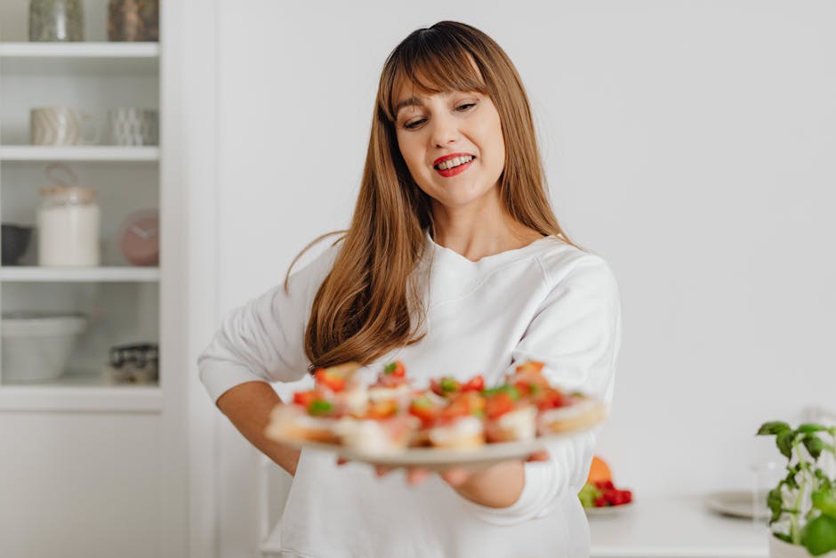 Smiling woman in a white top holding a plate of fresh canapés in a modern kitchen setting.
