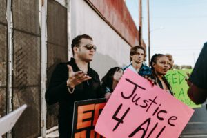 A diverse group of people holding signs advocating for justice and human rights in an outdoor protest.